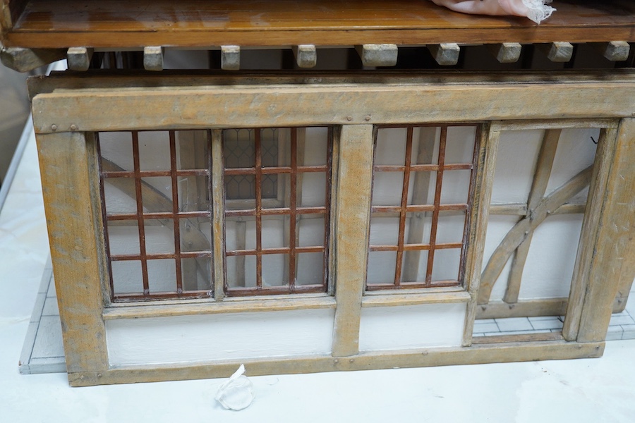 A modern doll’s house in the form of an oak framed Tudor house on three floors, with a shop on the ground floor, removable front panels on each floor and one side of the roof, with internal detailing and a good selection
